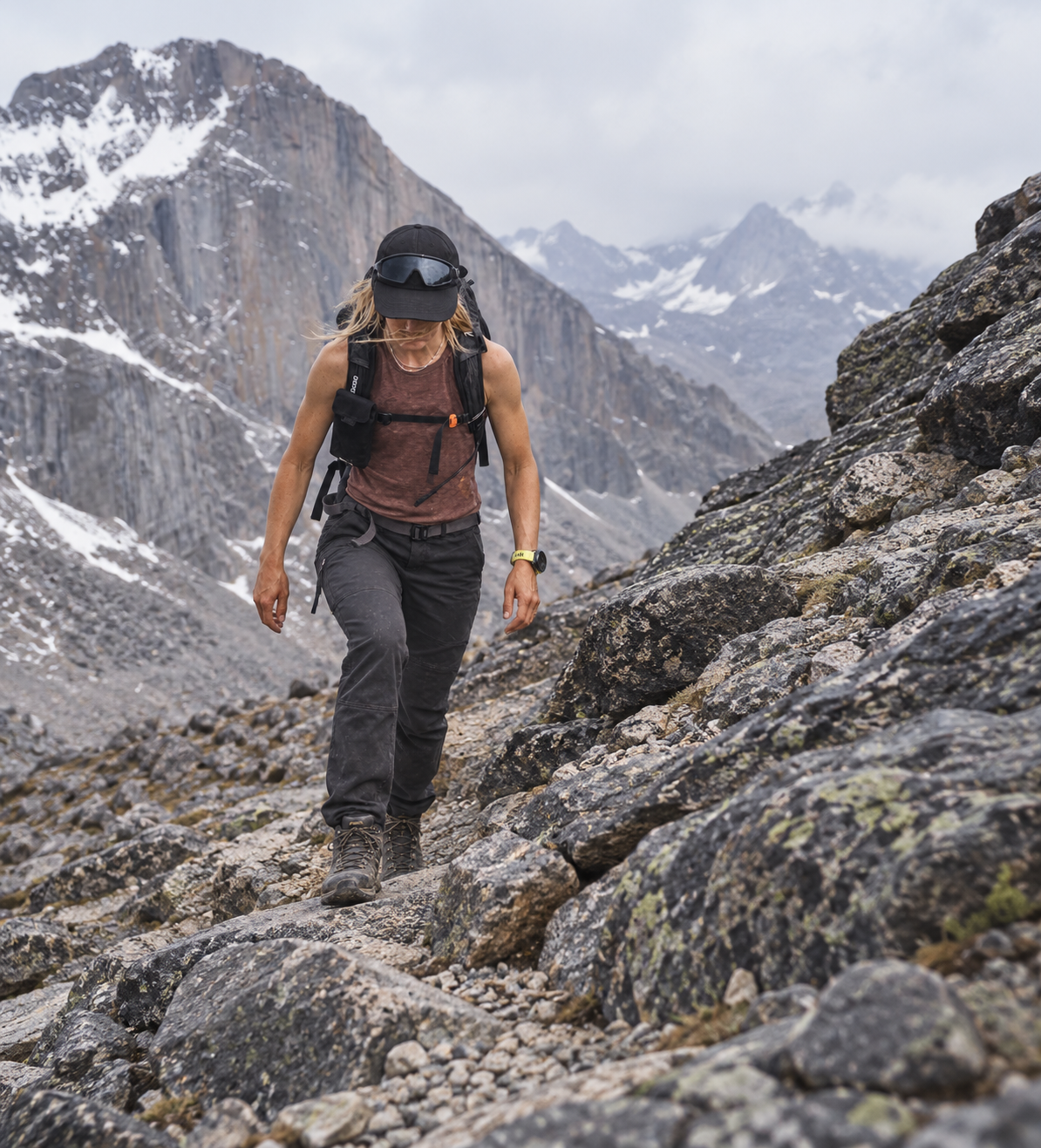 Hiker on a rocky alpine trail below a snow-streaked face